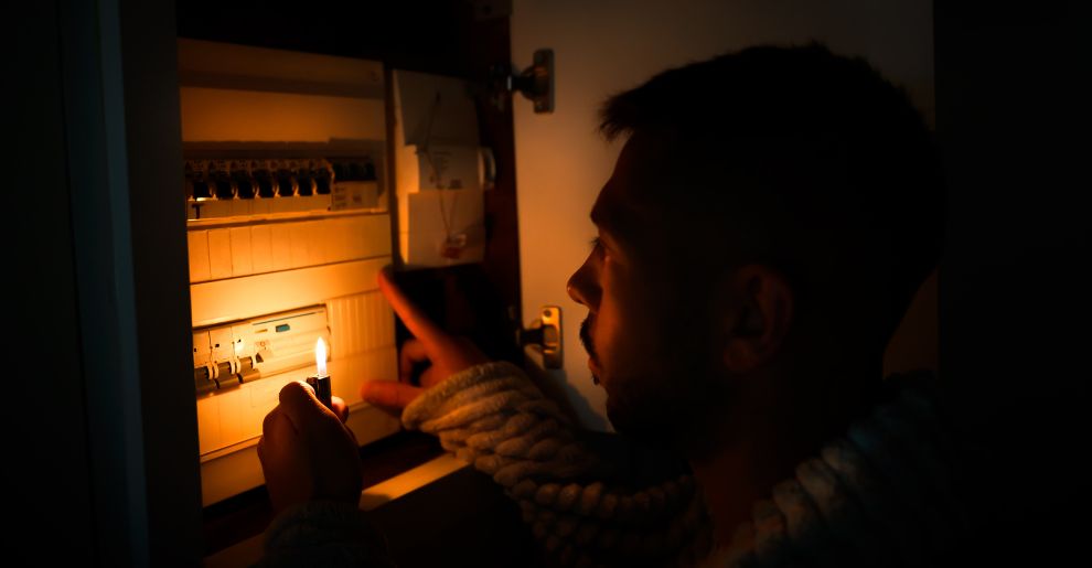 Man with lighter in total darkness investigating fuse box or electric switchboard at home during power outage. Blackout, no electricity concept - Bowling & Co Solicitors (1)